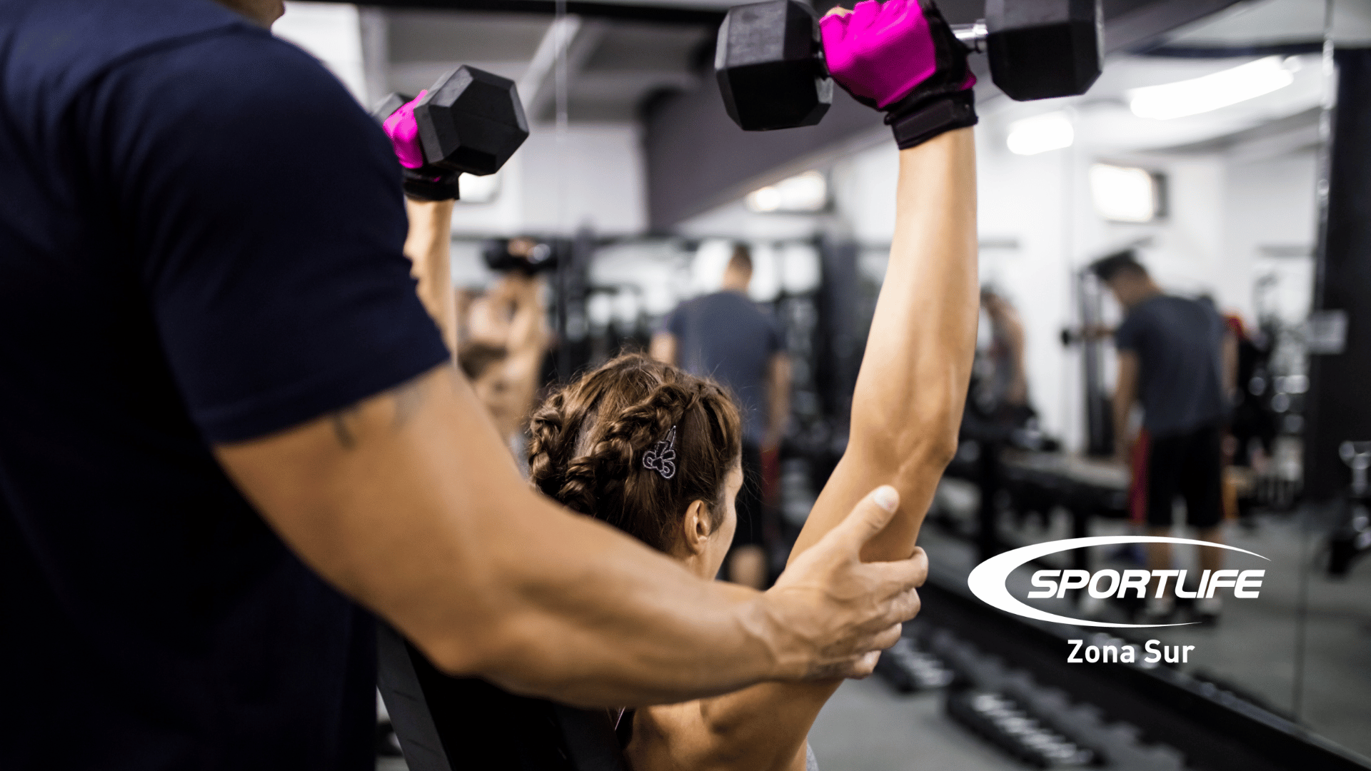 **Alt text:** Persona entrenando en el gimnasio de Sportlife Zona Sur, recibiendo indicaciones de un instructor para usar correctamente una máquina y evitar lesiones.